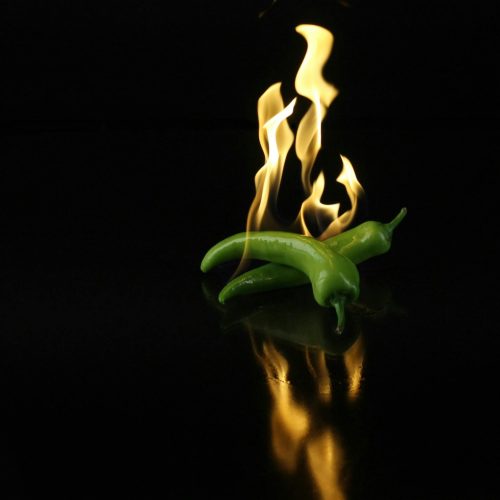 Dynamic image of green chili peppers engulfed in flames over a dark reflective surface.